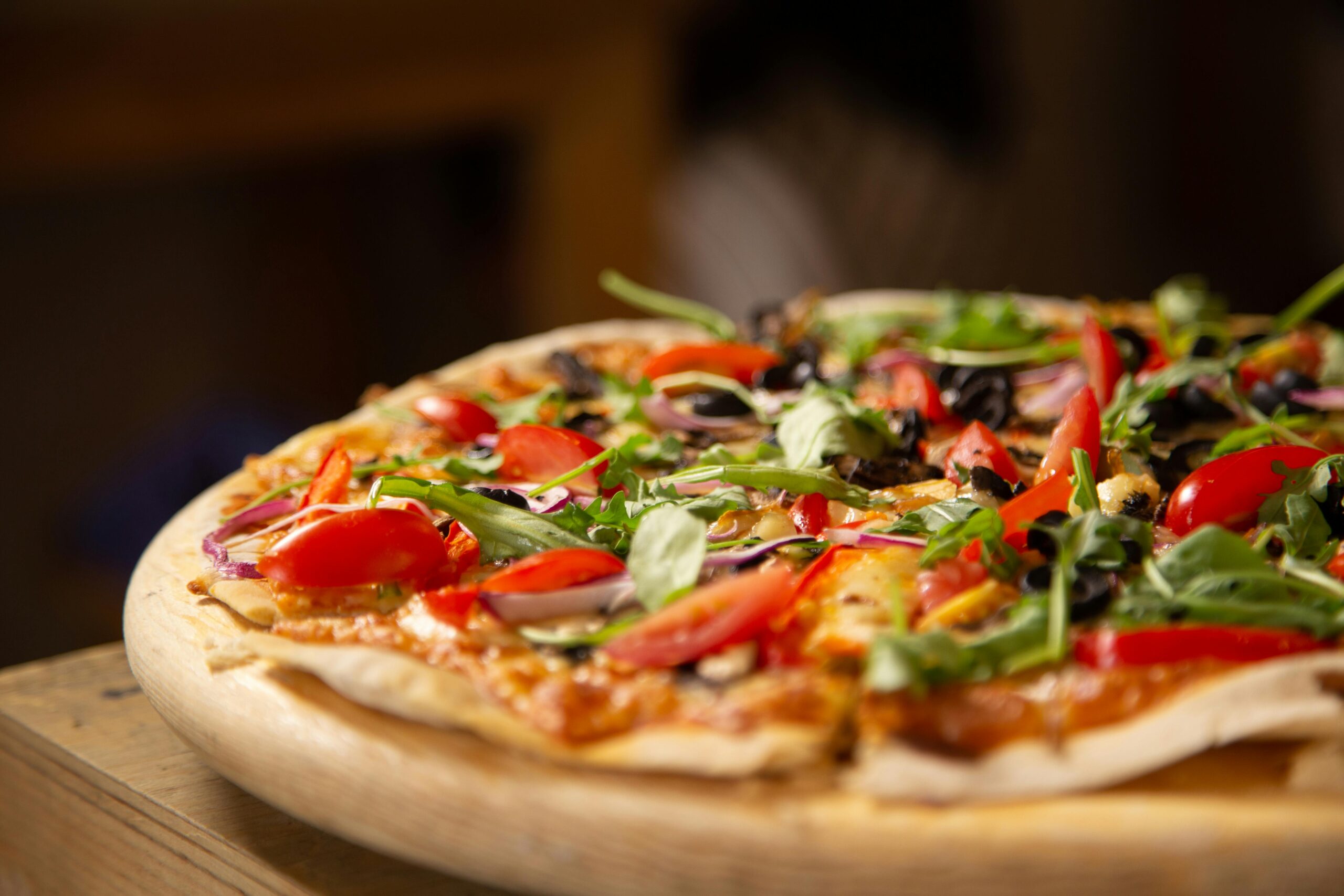 Close-up of a fresh vegetable pizza topped with arugula and cherry tomatoes on a wooden board.